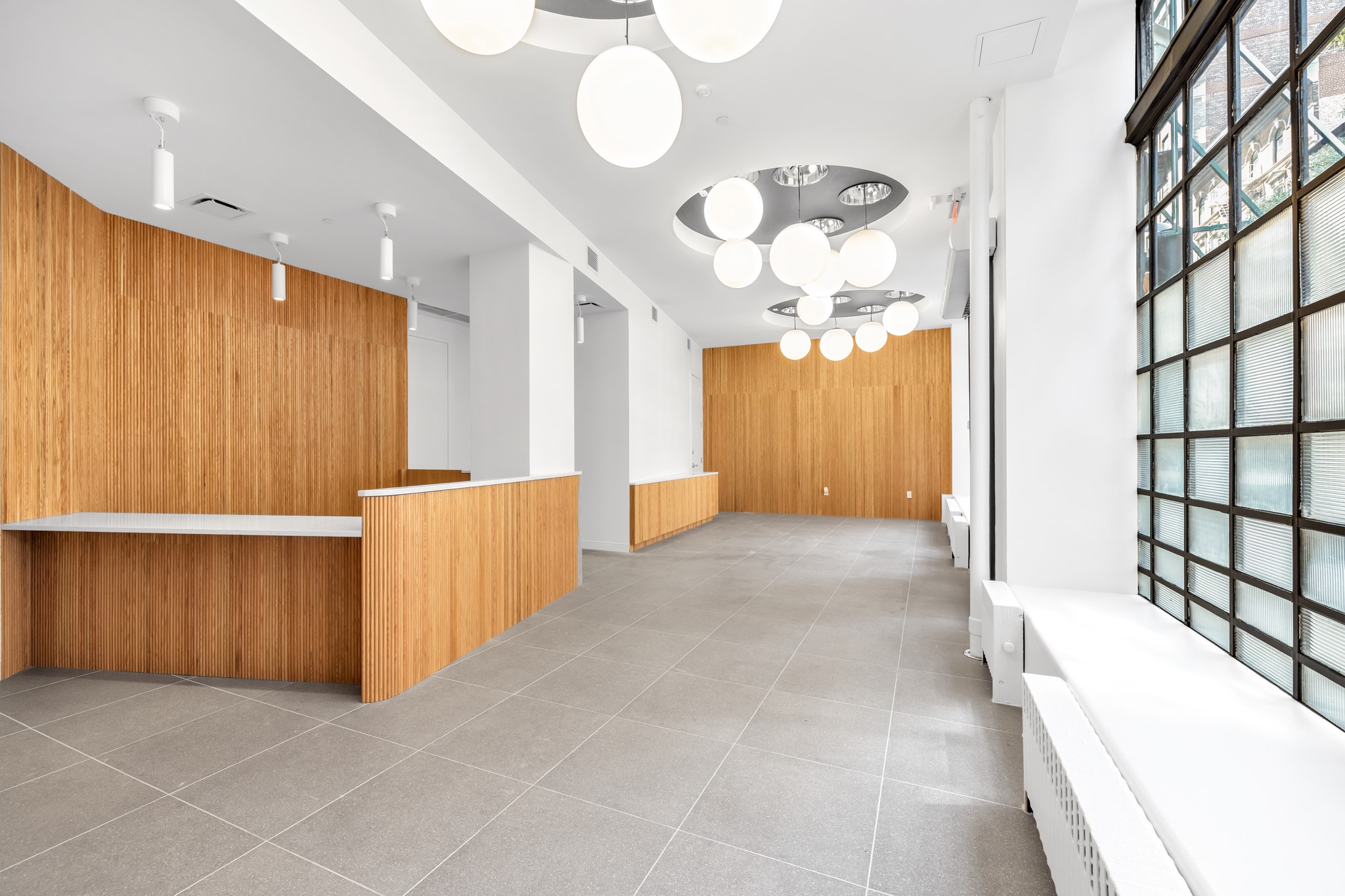 Empty office reception area with wood-paneled desk, corridor, and pendant lighting