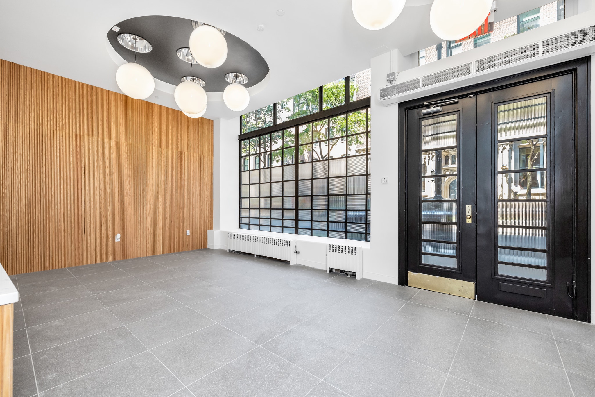 Vacant commercial space with wood paneling, black double entry doors, and large windows