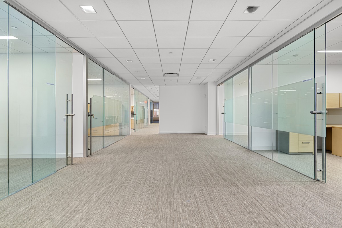 Corridor lined with frosted glass office partitions and neutral striped carpet