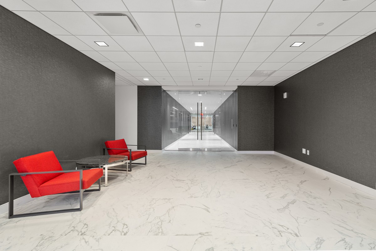 Reception lobby with red lounge chairs, dark walls, and marble floor leading to glass entry