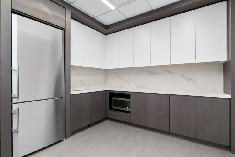 Corner kitchenette with white upper cabinets, dark gray lowers, and marble backsplash