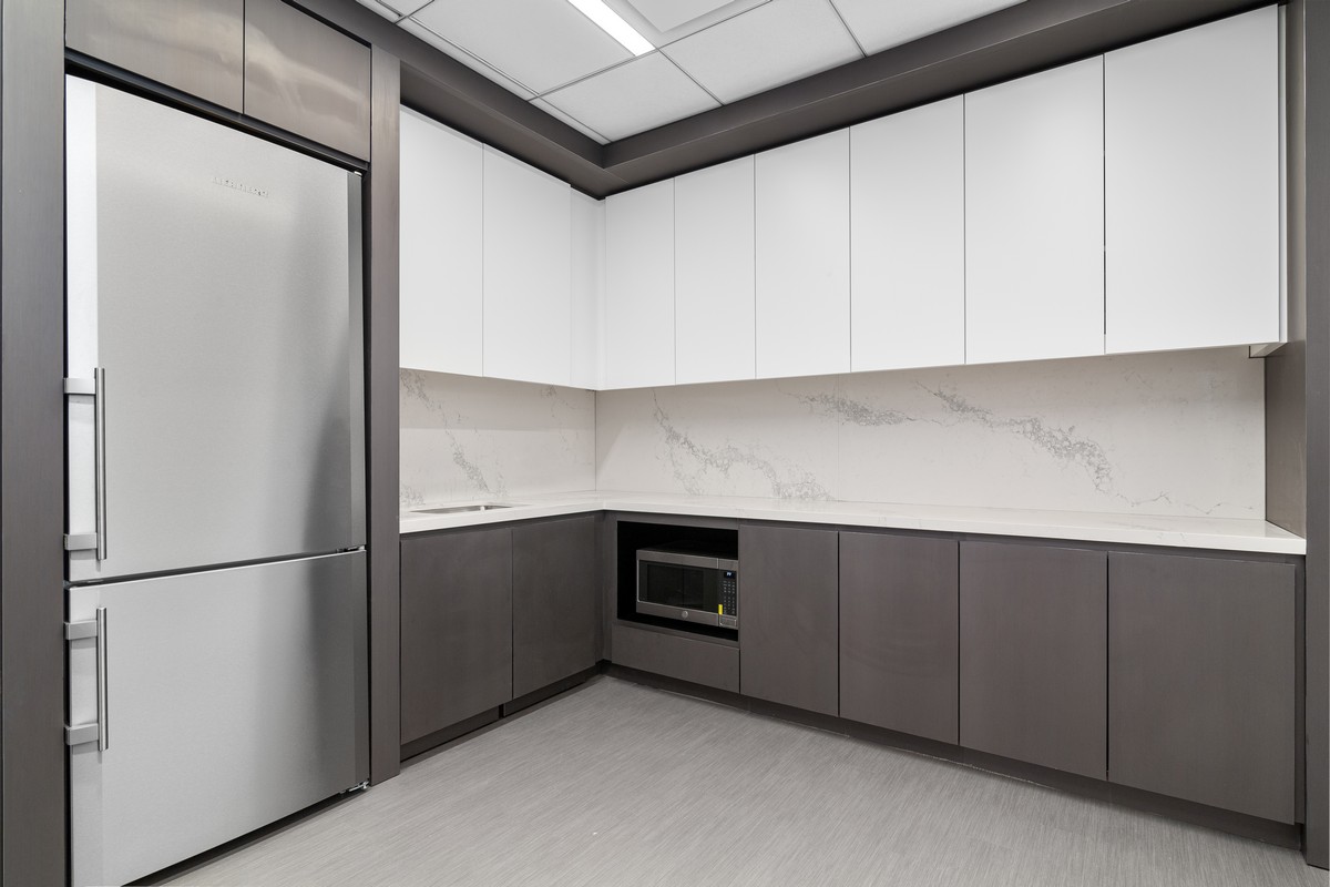 Corner kitchenette with white upper cabinets, dark gray lowers, and marble backsplash