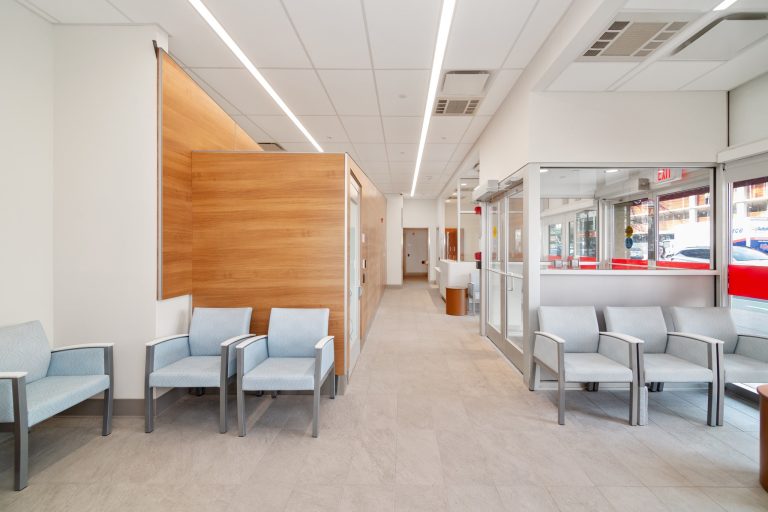 Waiting room corridor with wood accent wall, blue chairs, and street-facing glass entrance