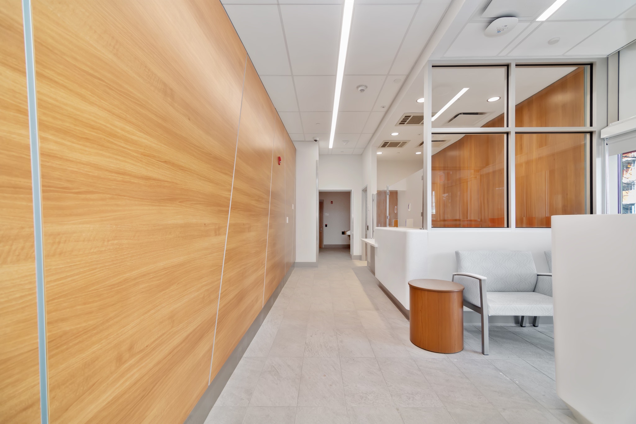 Corridor with light wood paneled wall leading to reception desk and seating area