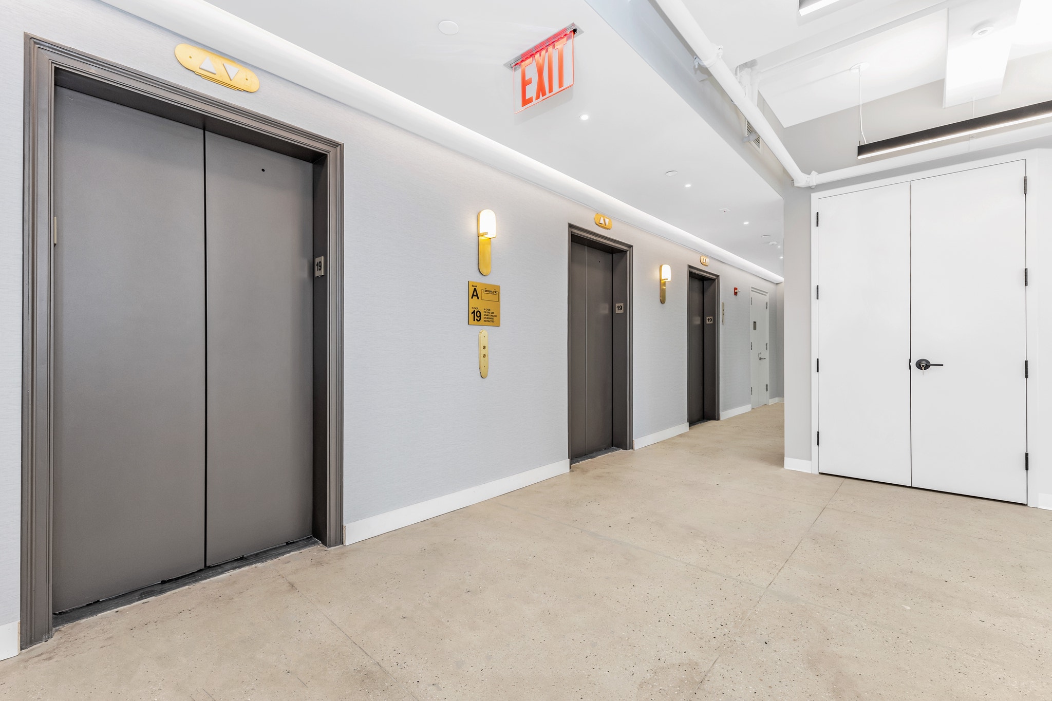 Elevator lobby on floor 19 with brass fixtures, dark doors, and illuminated exit sign