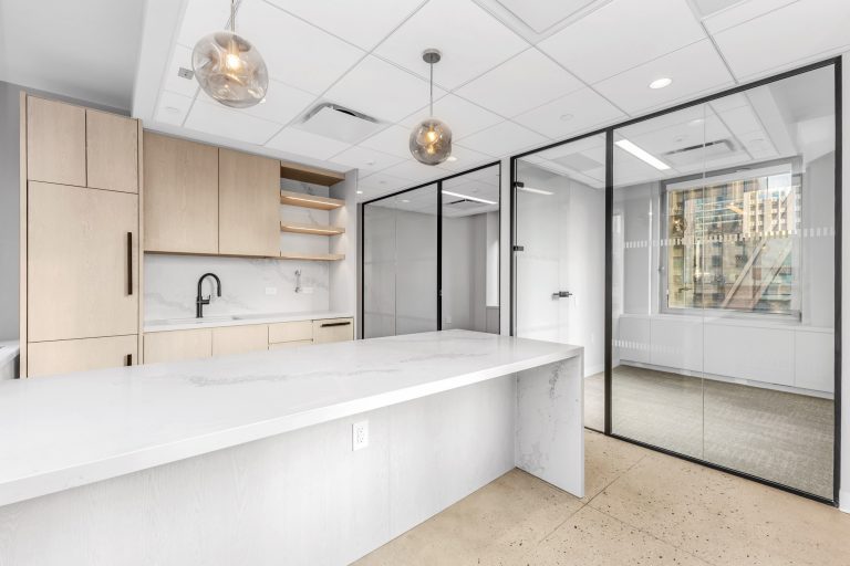 Office kitchenette with light wood cabinetry, marble backsplash, and glass pendant lighting