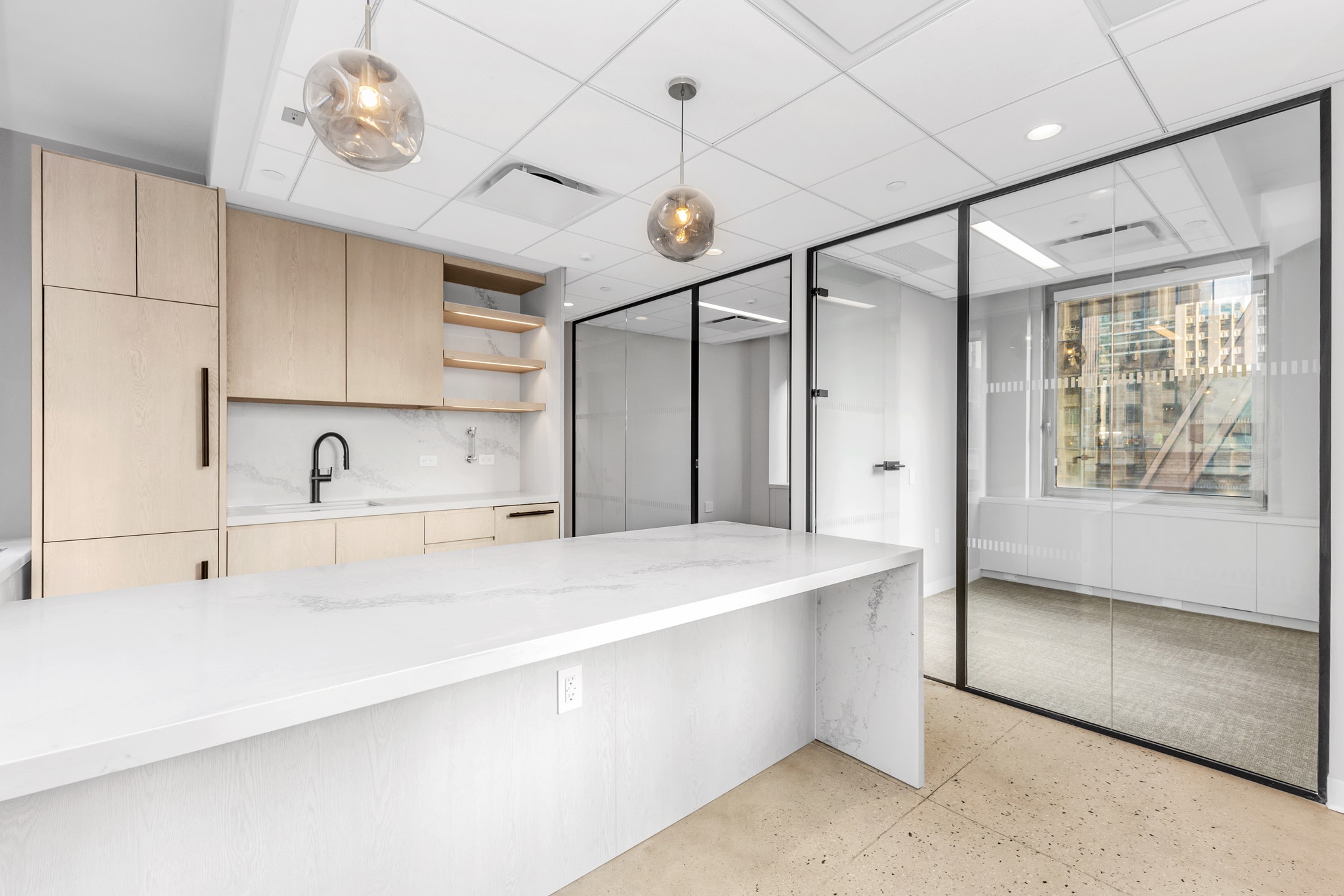 Office kitchenette with light wood cabinetry, marble backsplash, and glass pendant lighting