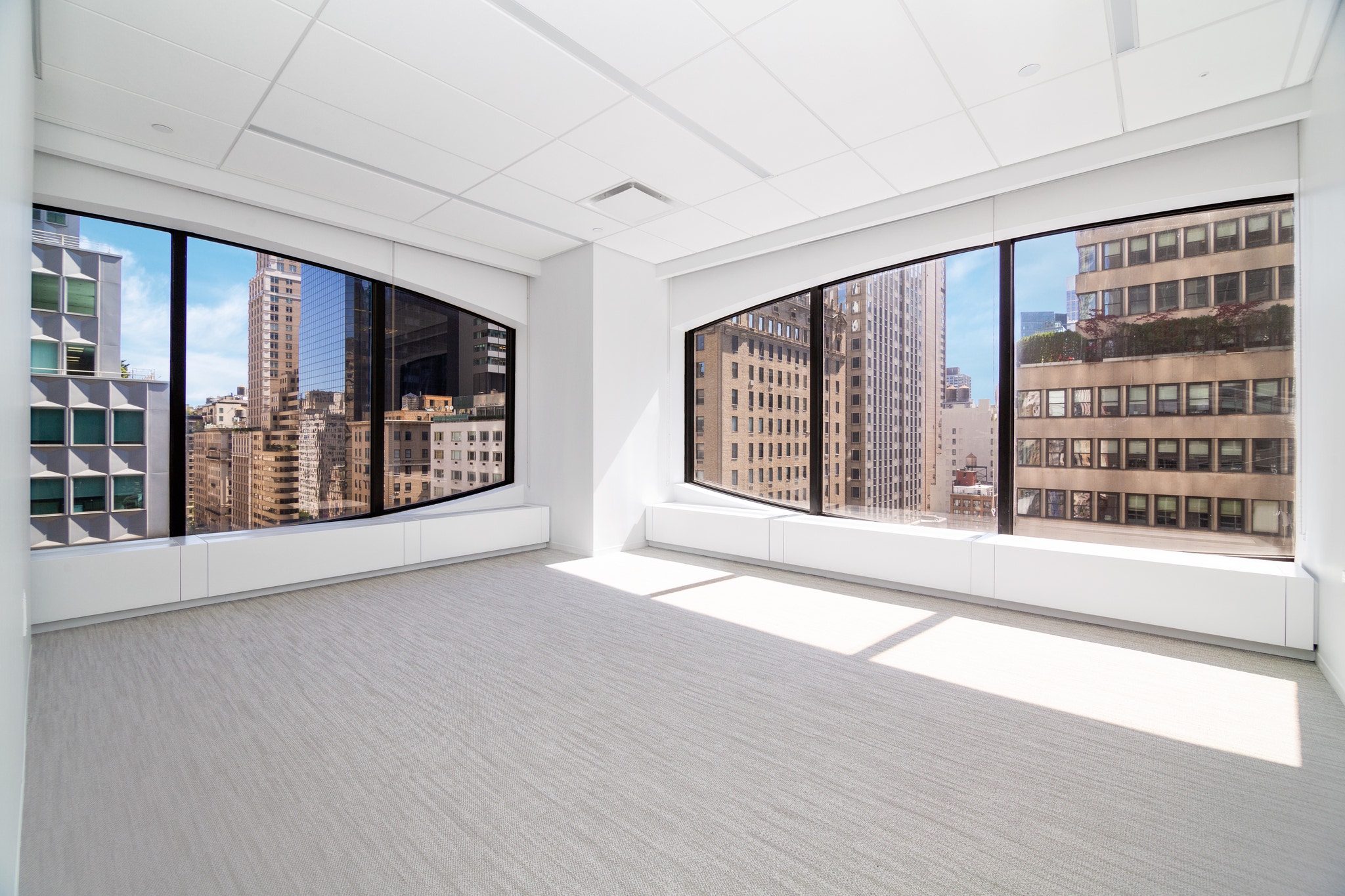 Empty corner office with curved black-framed windows overlooking dense Park Avenue skyline