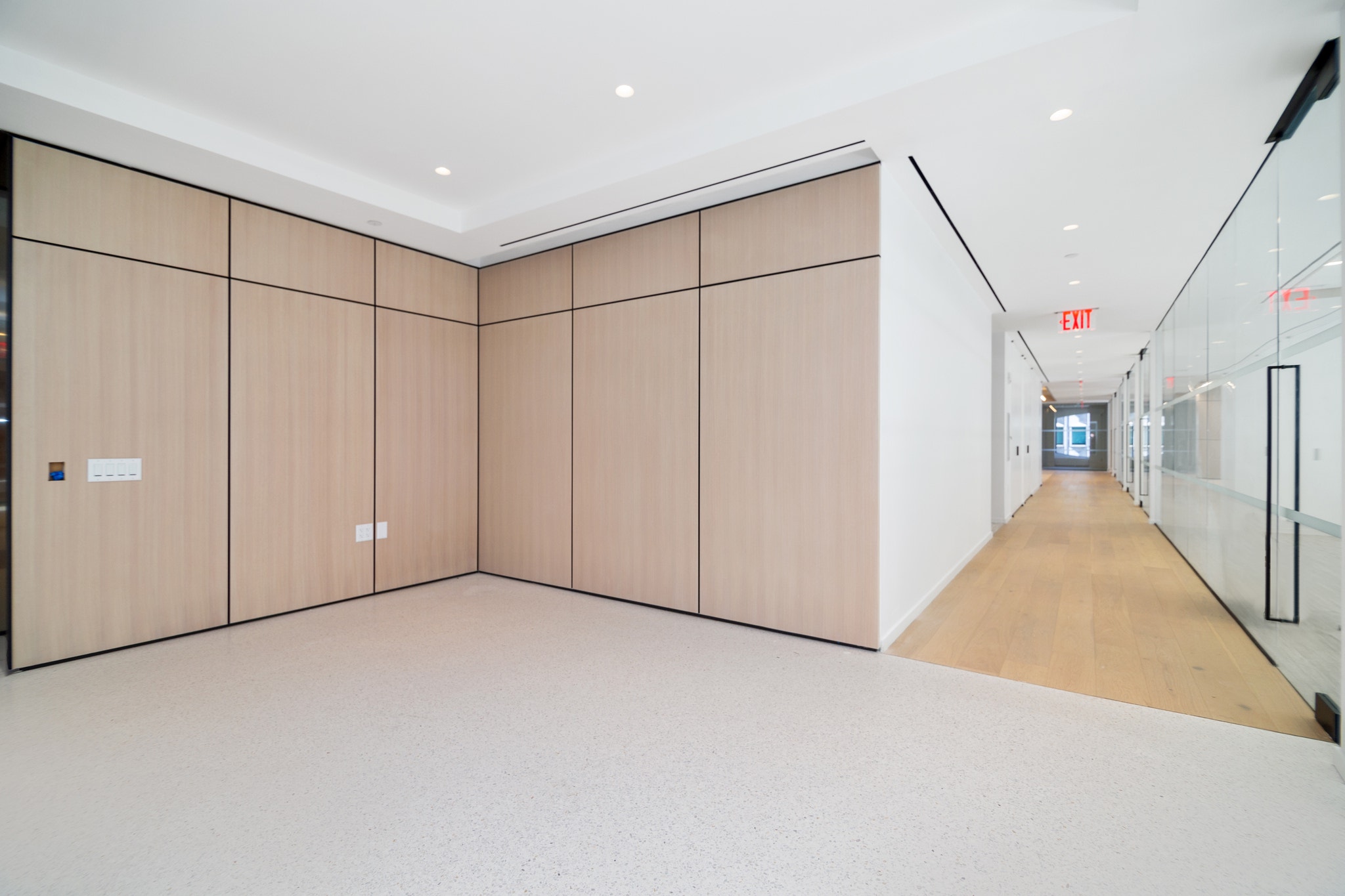 Wood-paneled corner room adjoining a glass-walled hallway with wood flooring