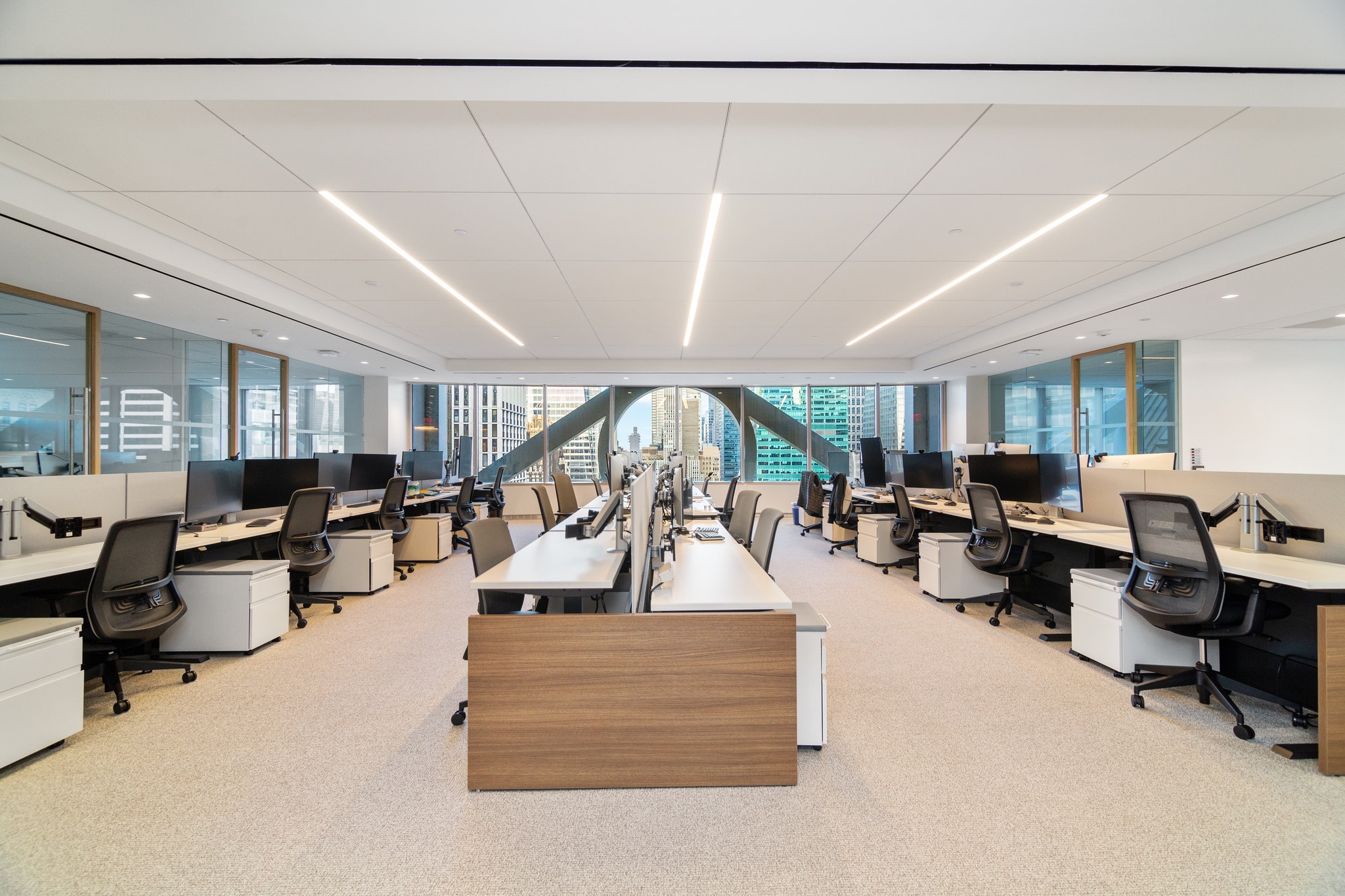 Open office bullpen with rows of white desks, dual monitors, and dramatic arched window views