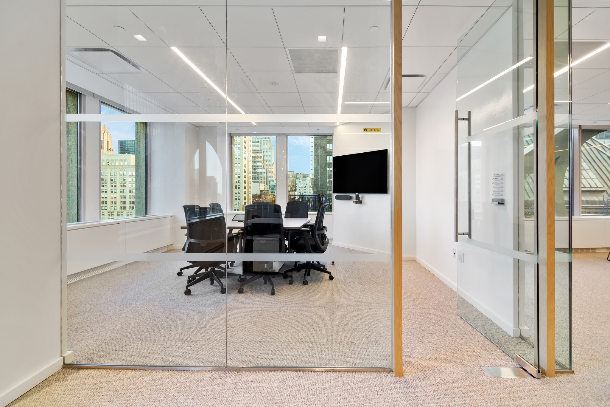 Glass-fronted conference room with black chairs, wall-mounted TV, and city skyline backdrop