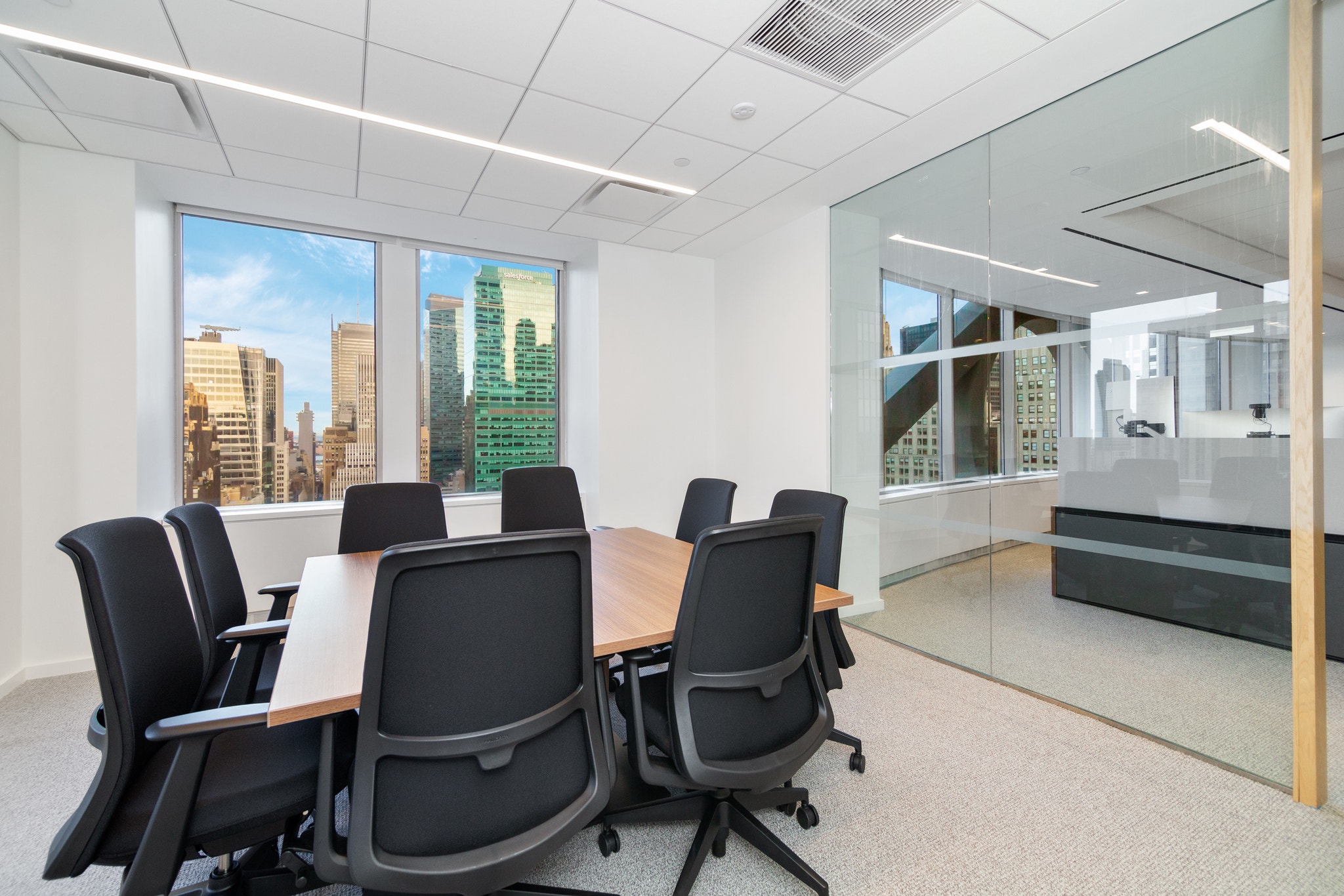 Small glass-walled conference room with black chairs, wood table, and city skyline views