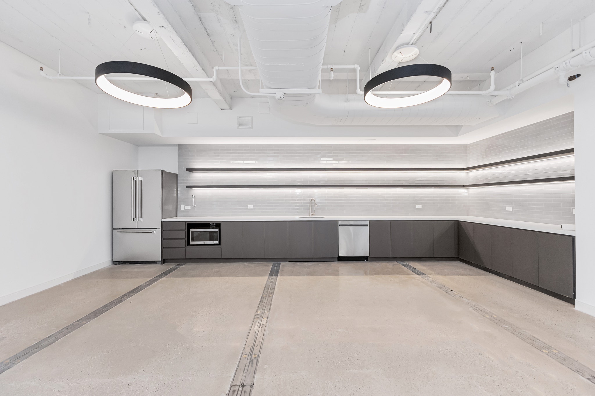 Office kitchenette with stainless fridge, gray cabinetry, subway tile backsplash, and ring pendant lights